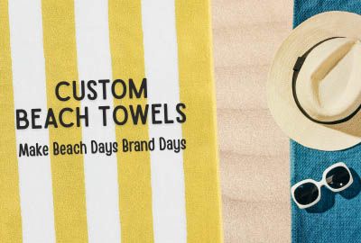 A custom logo beach towel laying on Canada's sandy Wasaga beach beside summer event swag.