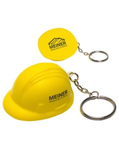 Two yellow coloured hard hat shaped stress relievers with silver coloured metal keychains and split ring attachments. The nearest hat is upright and has a black logo on the side. The hat behind it is turned to show the base with a black logo