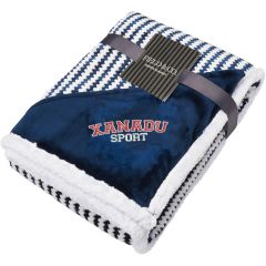 An angled view of a navy and white zig zag striped blanket folded up. In the corner there is a navy triangle of material with an embroidered logo on it 