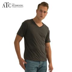 A charcoal heather coloured ring spun V-neck tee being worn by a short haired man with one hand in his pocket standing in front or a grey wall