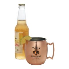 A 16oz copper and stainless steel moscow mule mug with black and orange logo in front of a bottle of beer