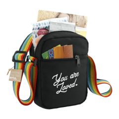 A black recycled crossbody tote with a rainbow strap. There is a white custom logo on the front and the bag is filled.