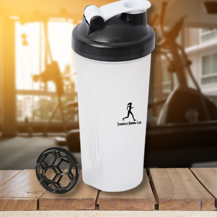 A 600mL black and clear cross trainer shaker bottle on a wooden table with a gym interior in the background.