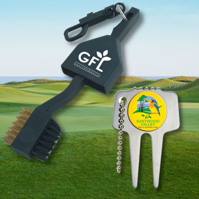 A black golf brush and stainless steel divot repair tool laid over a freshly cut golf course that is overlooking the coastline.