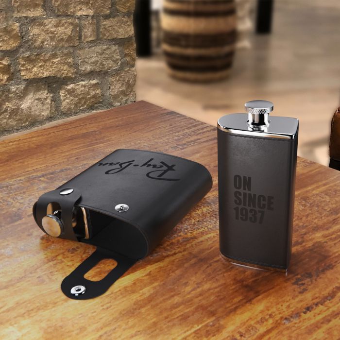 An angled view of a black dual flask resting on a wooden table inside of a modern log-cabin style brewery's taproom.