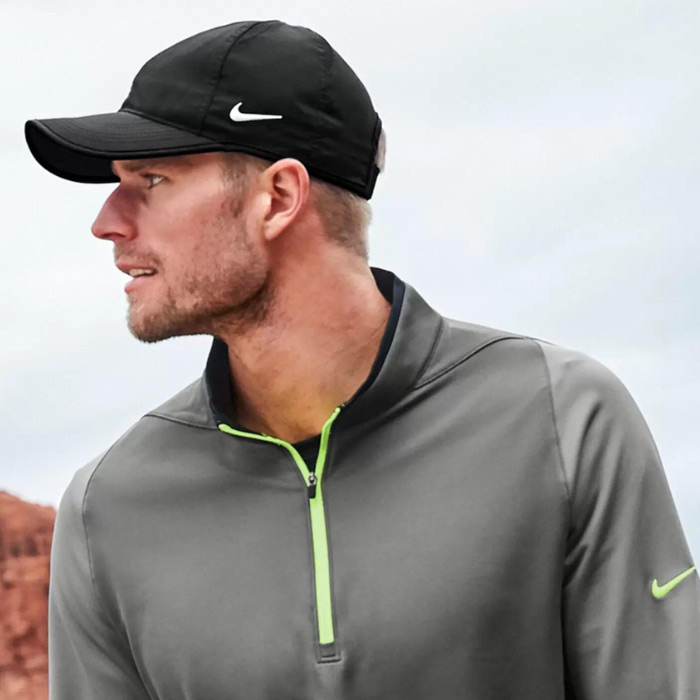 A man wearing his grey Nike windbreaker and black Nike ballcap just after hitting a great shot at an Arizona golf course.